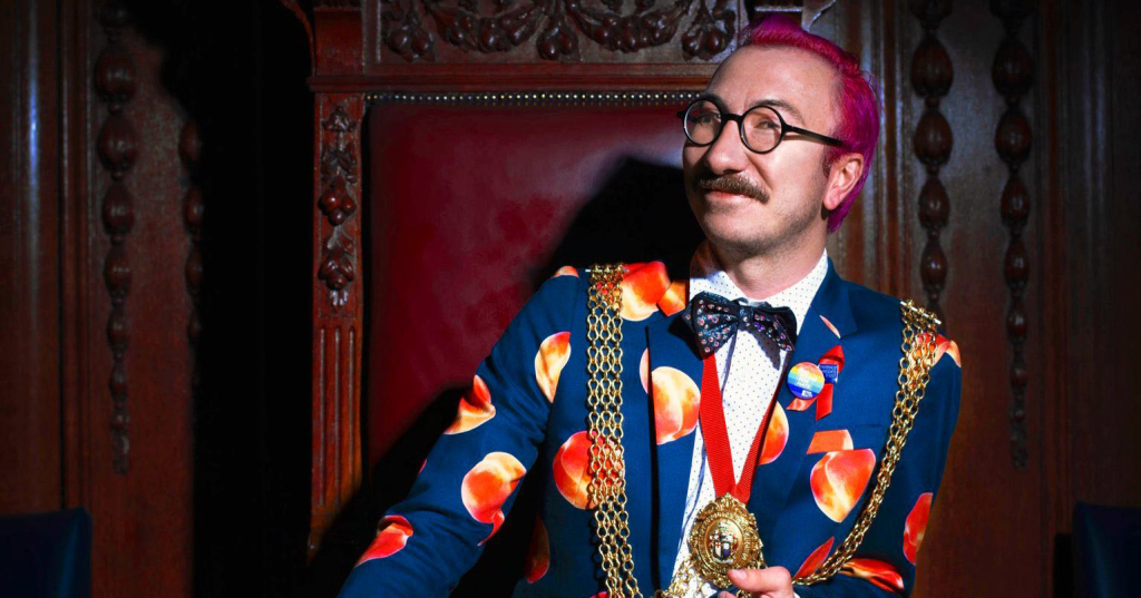 A brightly dressed smiling man sitting on a throne