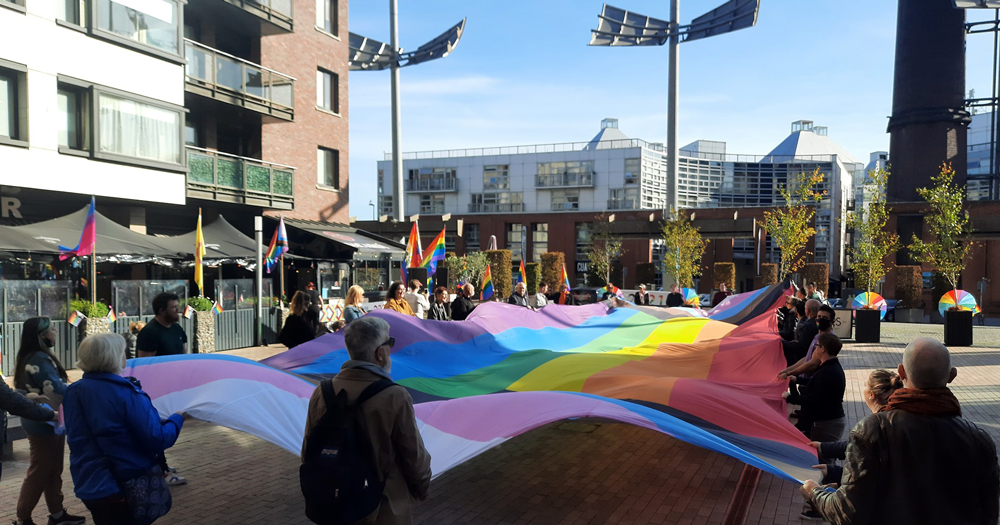 People in a city square unfurling a gigantic rainbow flag