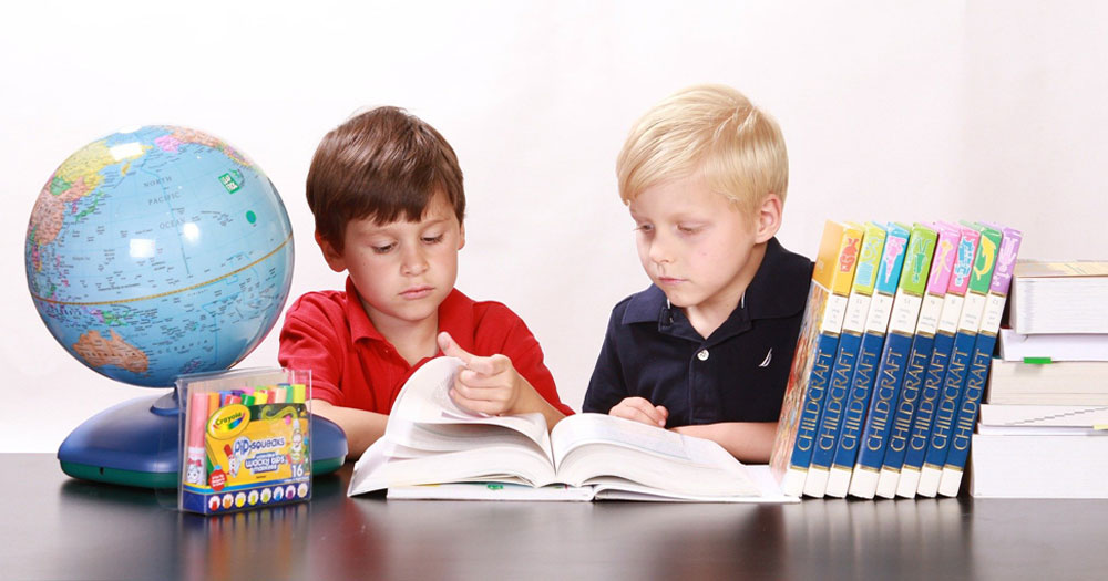 Two young boys sitting at a desk reading a book together. There's a globe on the left and a stack of books on the right. This story details the National Anti-bullying Action Plan in Ireland.