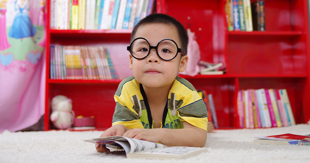 A little boy with glasses reading in his room