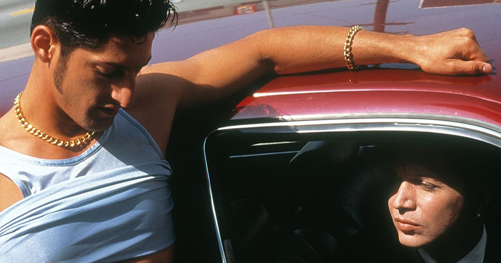 A hustler leans against a car while filmmaker Bruce LaBruce peers from the driver window