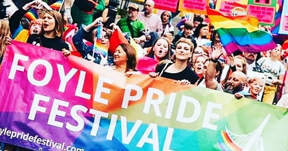 People marching with a "Foyle Pride Festival" banner and rainbow flags.
