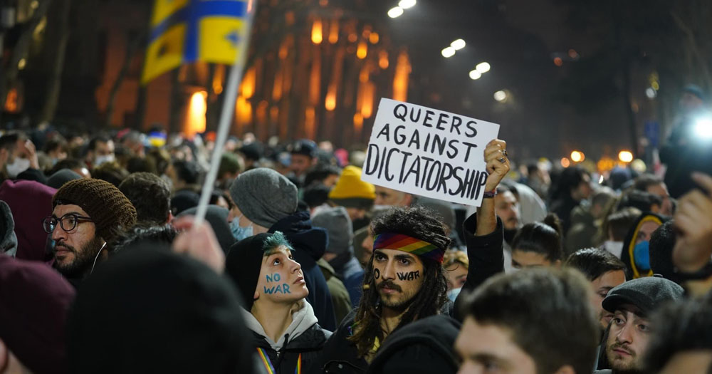 OutRight launch vital new Ukraine LGBTQ+ fund. The photograph is of a night time demonstration with people wearing blue and yellow in support of Ukraine/ the two people in the centre have the words 'No War' painted on their faces and are carrying a placard which reads 