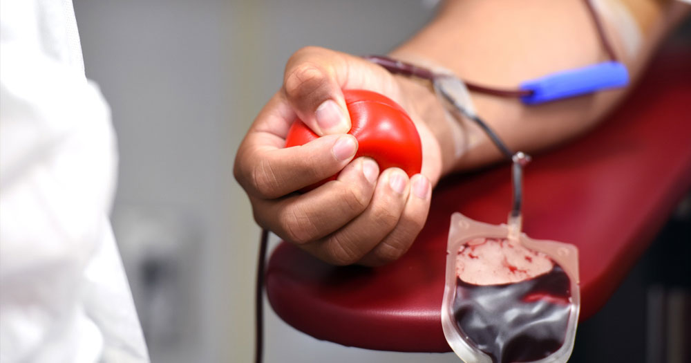 Close up of hands squeezing a red ball as someone donates blood