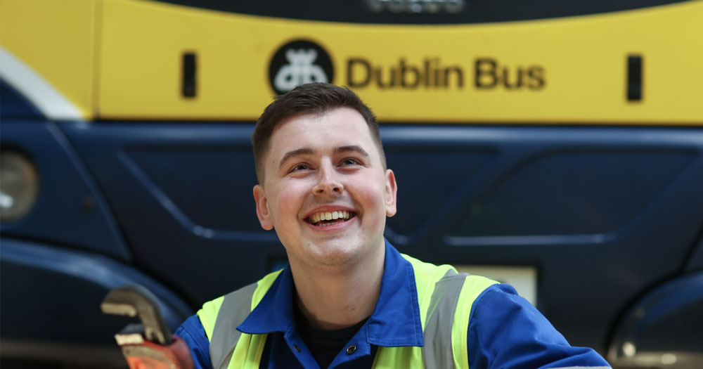 Dublin bus team member smiling and wearing a high vis jacket in front of a Dublin bus