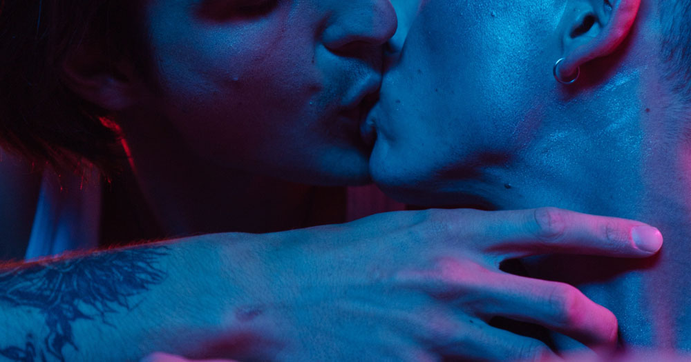 HIV Ireland have launched their report looking at sexual health during the COVID pandemic. The image shows the lower part of two men's faces as they kiss. One man is running his arm across the neck of the other.