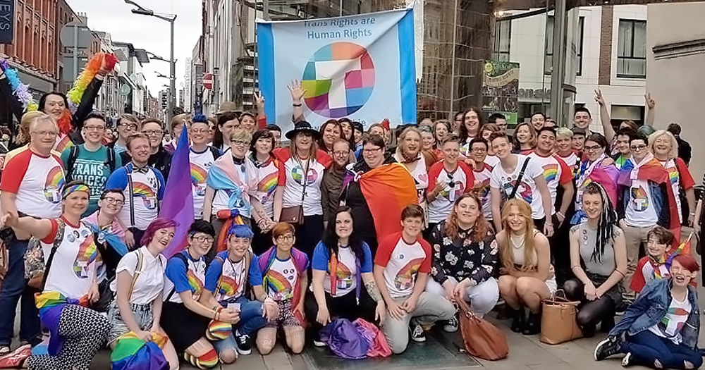 A group of smiling people wrapped in Trans flags