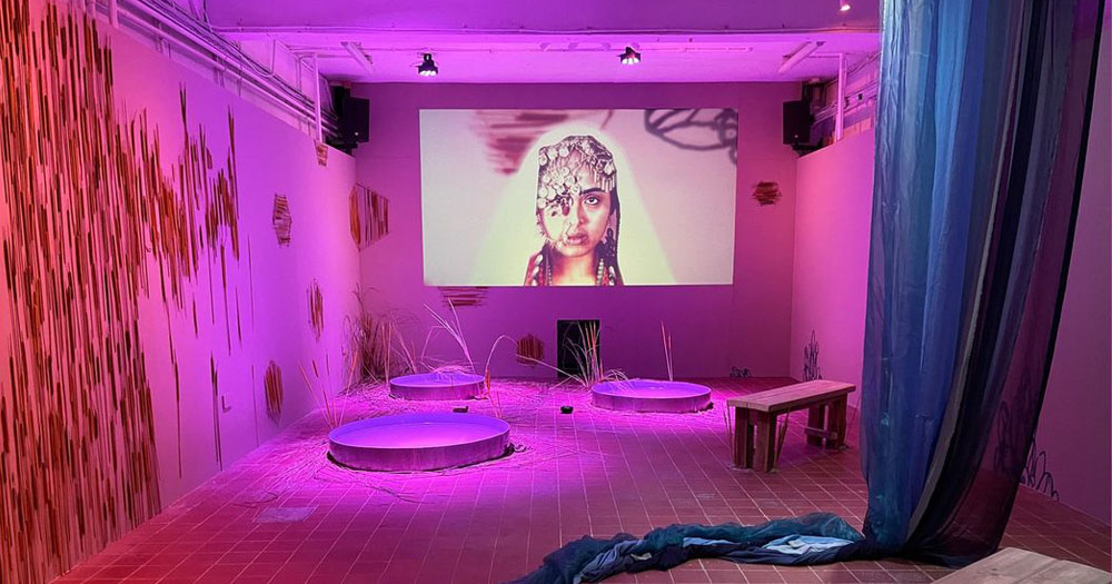 A4 Sounds have an open call for an artist residency. The photograph shows work by Rima Hamid as part of the 'We Want the Earth' Programme. The photograph is of a room in pink light with a wall projection of a woman with an India style headdress.