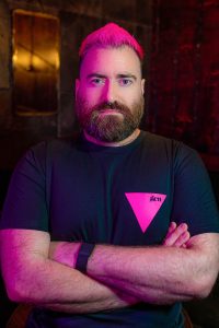 A model looking at the camera wearing a black T-shirt with a small pink triangle.