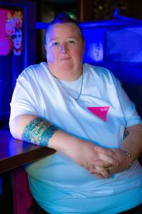 A model looking at the camera wearing a white T-shirt with a small pink triangle.