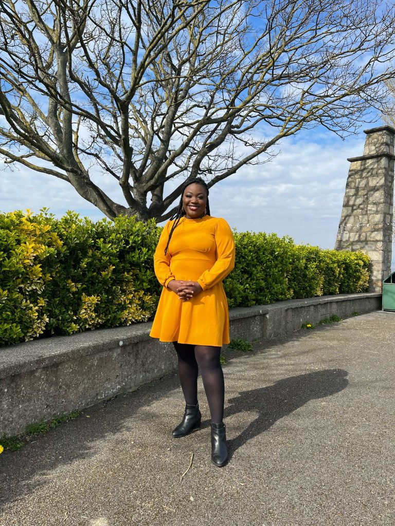 Zainab Boladale poses outdoors on a sunny day in a yellow dress.