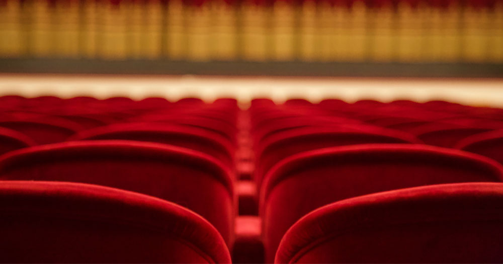The International Dublin Theatre Festival 2022 returns to theatres. The photograph shows a close up over the top of red theatre seating with a sorf focus stage curtain in the the background.
