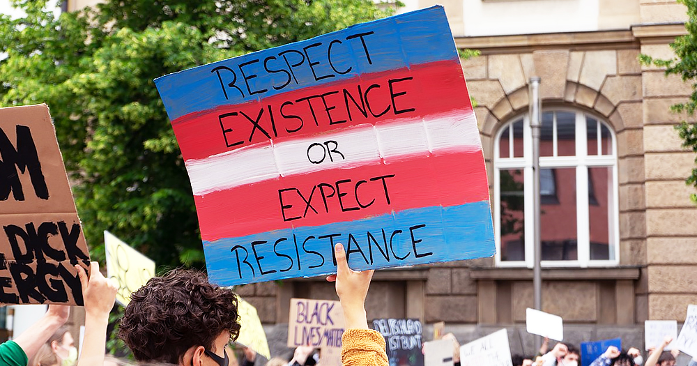 Protestor holds up a Trans sign reading "Respect Existence or Expect Resistance" as LGBTQ+ groups boycott UK event.