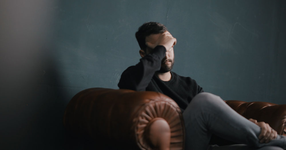 Report finds that LGBTQ+ people are often blamed for their own child sexual abuse. The photograph shows a man sitting on a couch with his hand covering his eyes.