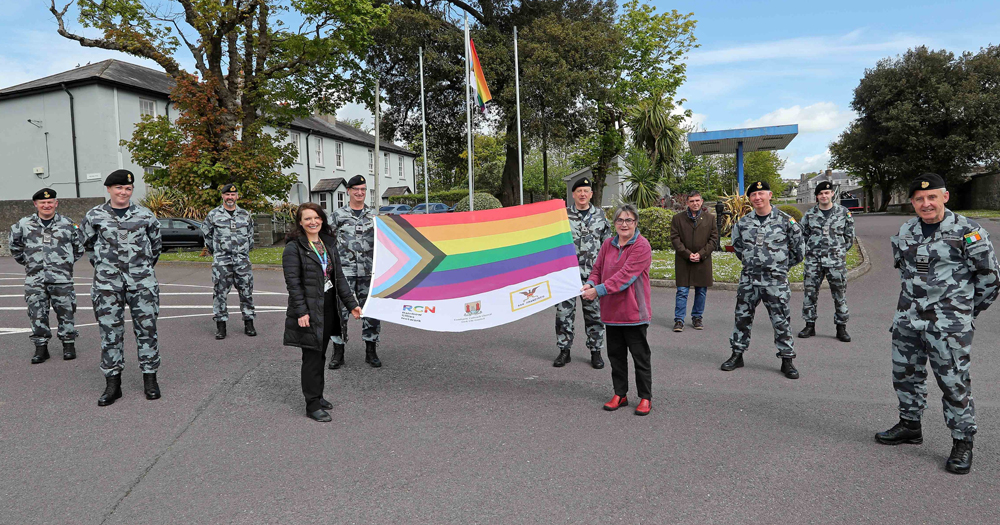Members of the defence forces at the launch of the Cork LGBTQ+ Awareness Week 2021. The photograph shows ten people standing to attention in military attire holding a progressive Pride flag.