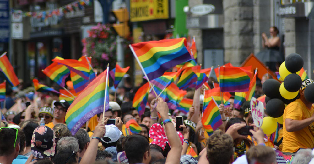 People waving dozens of rainbow flags as part of a Pride parade