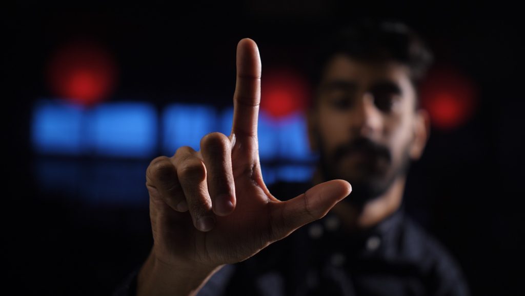 an image of a person holding their fingers in the shape of an L. Their hand is in focus but their face is blurred.