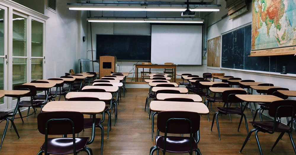 Empty classroom with single desks, blank blackboard, projector screen and a map on the wall. This story details Stella O'Malley giving a talking 