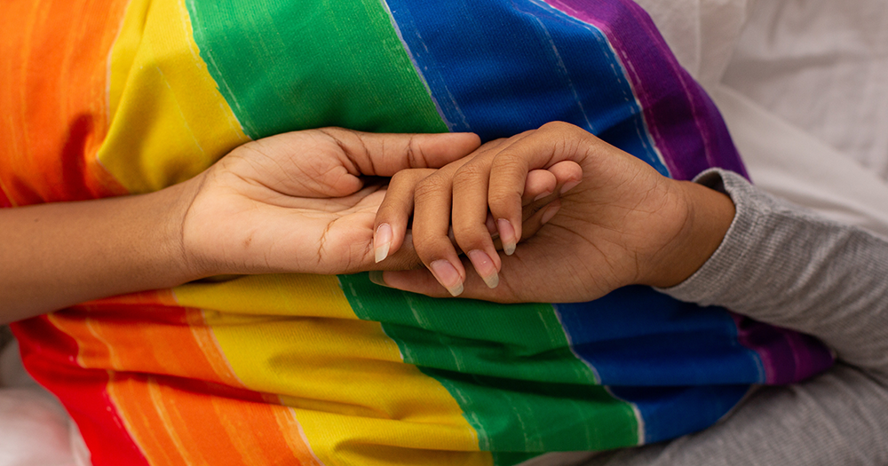 Two hands holding each other on top of a rainbow coloured pillow
