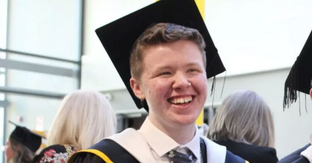 Mid-shot of a young man smiling off-camera, wearing a graduation cap and robe: Callum