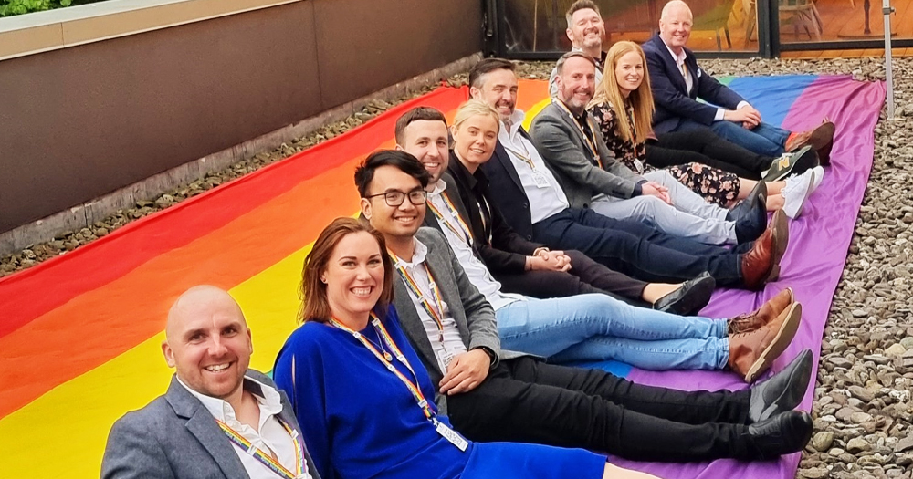 Members of the network Work With Pride for LGBTQ+ professionals, sitting on a rainbow flag.