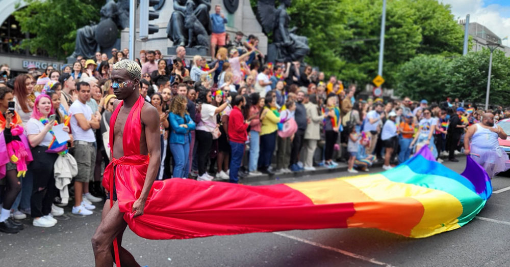One of the Dublin Pride parade 2022 marchers, wearing a red outfit that flows into a long rainbow flag train