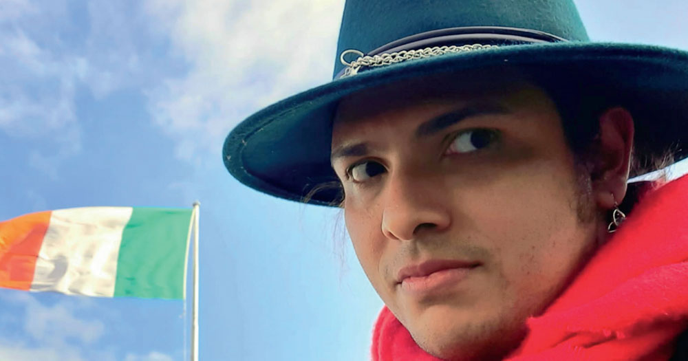A photograph of one of the participants from the International Protection research conducted by LGBT Ireland the Irish Refugee Council. The photograph shows a man wearing a traditional South American hat with a red scarf. In the background is an Irish flag.