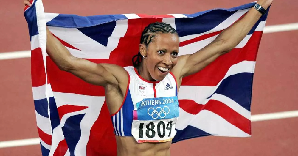 Image of Olympian Kelly Holmes running with England flag behind her.