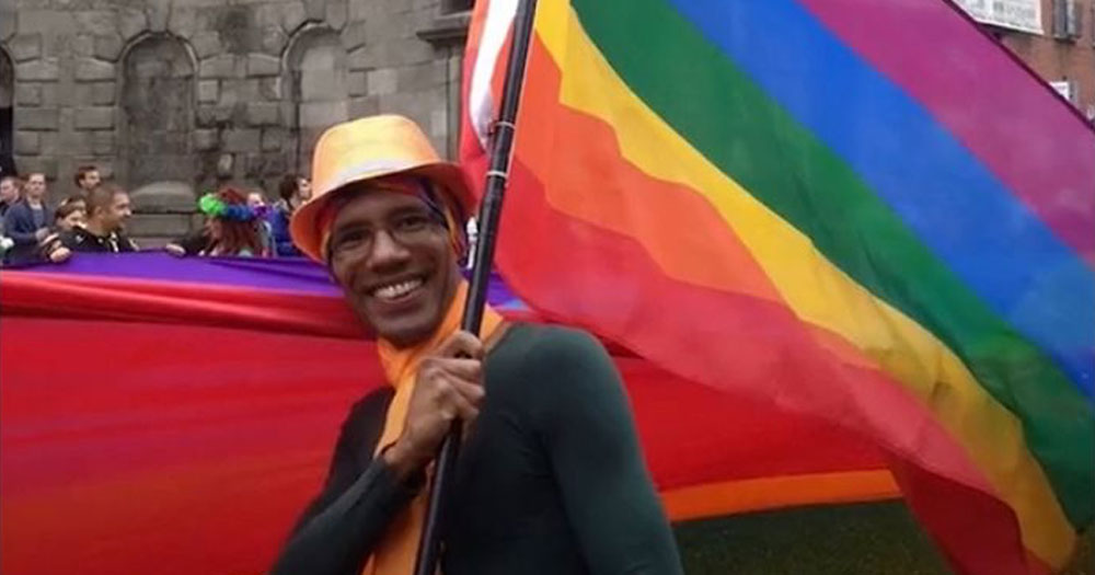 Marlon Jimenez-Compton smiling and waving a rainbow flag at a Pride parade