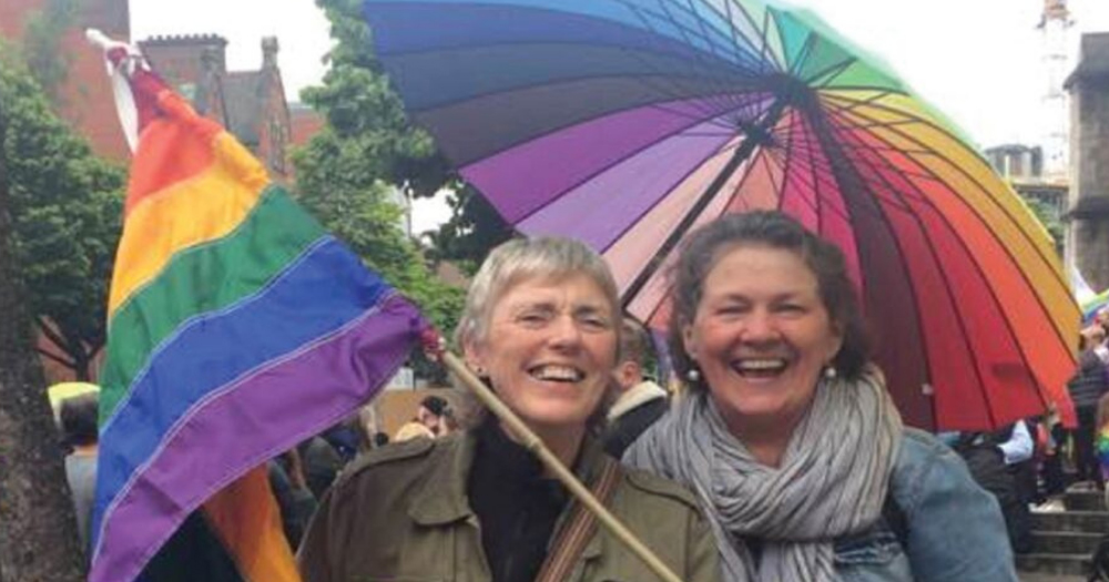 Image of two women posing with a rainbow flag and umbrella.