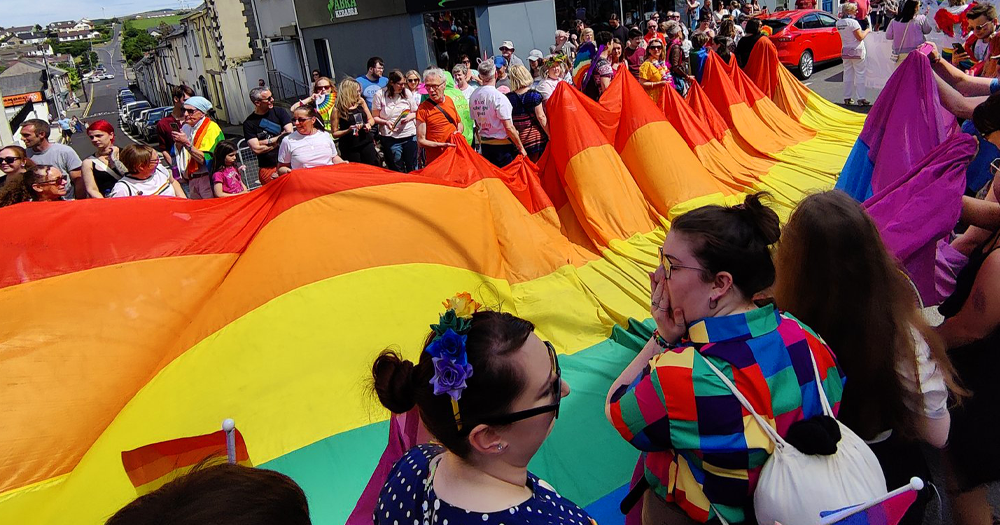 Irish Pride events taking place in Inishowen. Attendees are holding a long rainbow flag in the street.