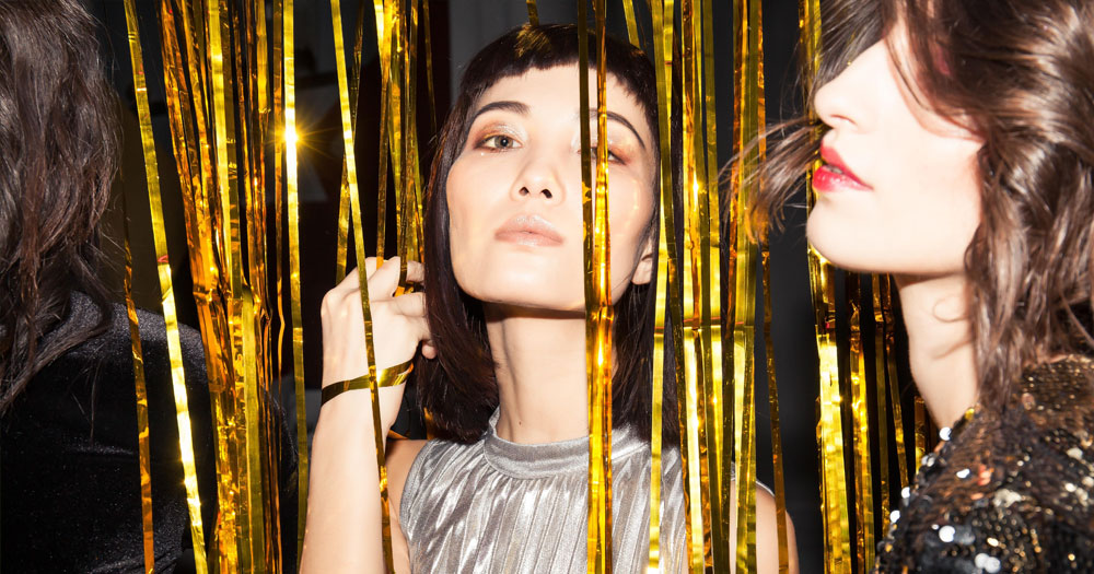 A woman in a disco dress peers out from behind a tinsel curtain
