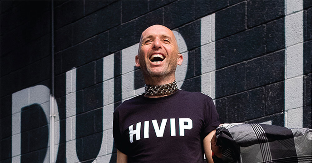 A smiling bald person wearing a HIVIP shirt