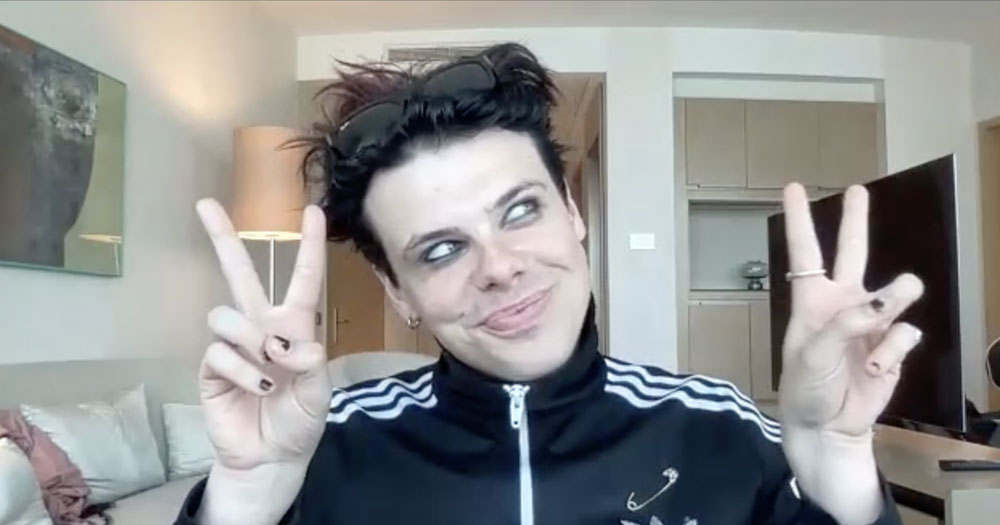 Close up of Yungblud smiling and giving peace signs with his hands from a hotel room in Poland
