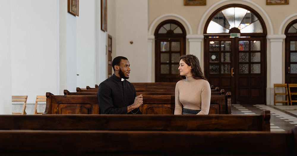 A priest speaks to a young woman on a church pew. The Irish Association of Catholic Priests supports a ban on conversion therapy, according to a July 16 blog post.