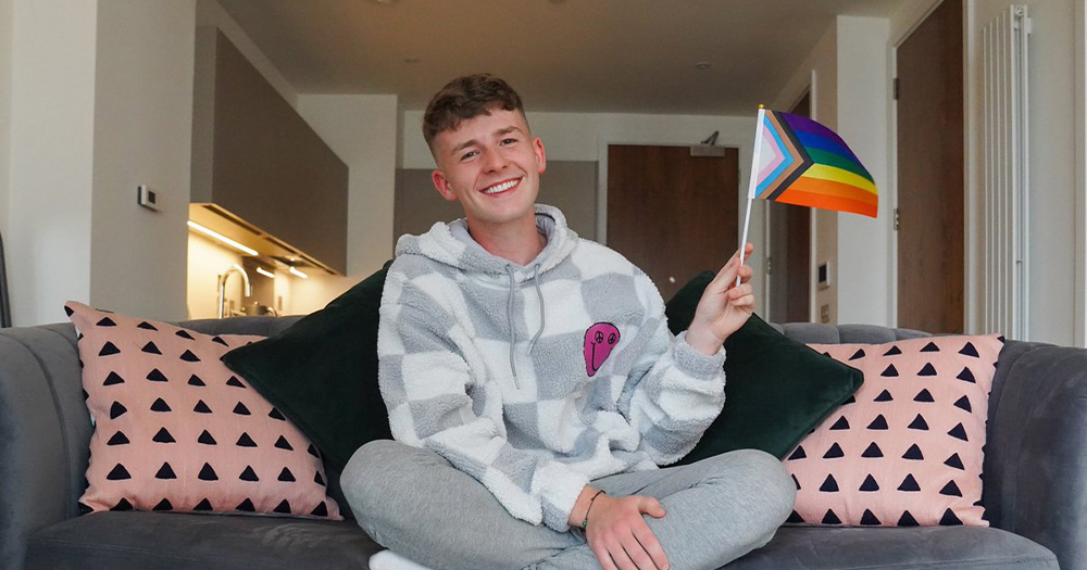 A photo of Adam B holding a pride flag and smiling.