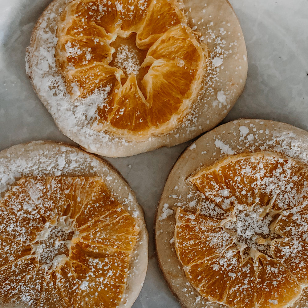 Three sugar cookies arranged neatly with a slice of orange and powdered sugar on top.