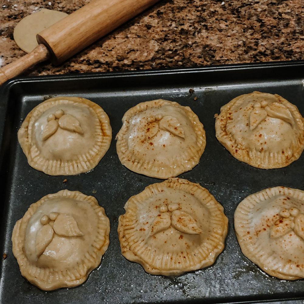 6 pastries aligned on a baking sheet, a rolling pin and flour laid behind them.