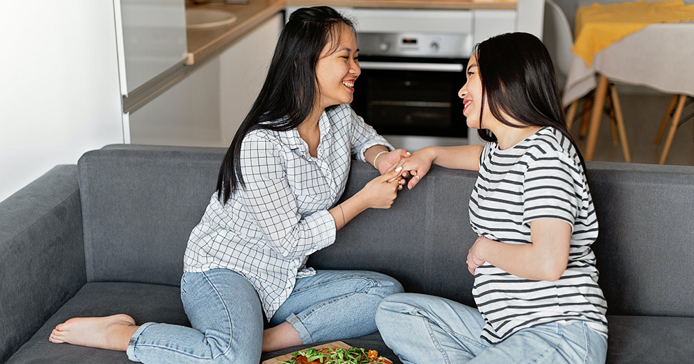 A lesbian couple on a couch, one of whom is pregnant. The NHS has just lifted its discriminatory requirements for same-sex couples to access fertility treatments.