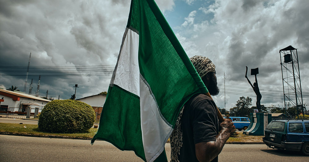 A man carries the flag of Nigeria over his shoulder and he walks down as street