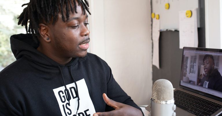 A man gestures with his hands as he speaks in front of a home podcasting set up with a microphone and computer. A new podcast that premiered this week will explore the experiences of immigrants in Ireland.