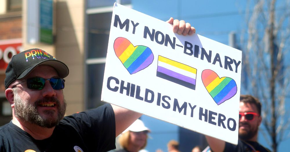 Close-up of a man holding a "my non-binary child is my hero" sign to illustrate ShoutOut's guide for parents of LGBTQ+ children