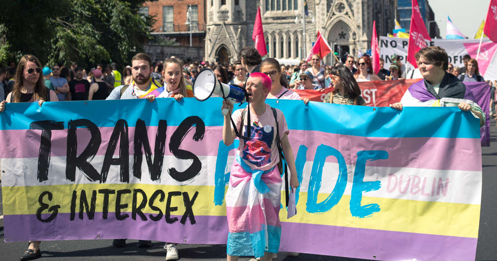 People marching at Dublin Trans and Intersex Pride, holding a banner and flags.