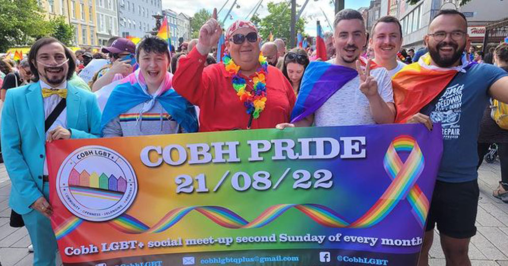 The photograph shows a group of five people wearing Pride and Trans flags carrying a banner which reads "Cobh Pride 21/08/22".