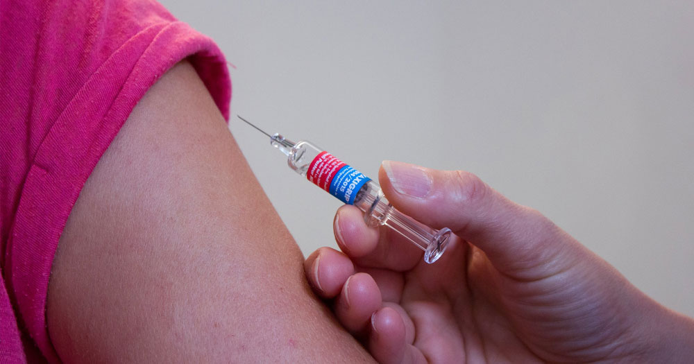 Close up of a hand injecting a vaccine into someone's upper arm
