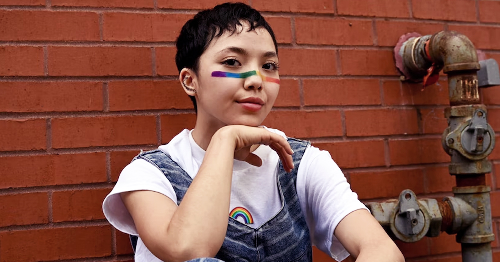 This article is about non-binary lesbians discussing inclusivity. In the photo, a person looking at the camera with a rainbow painted on their face.