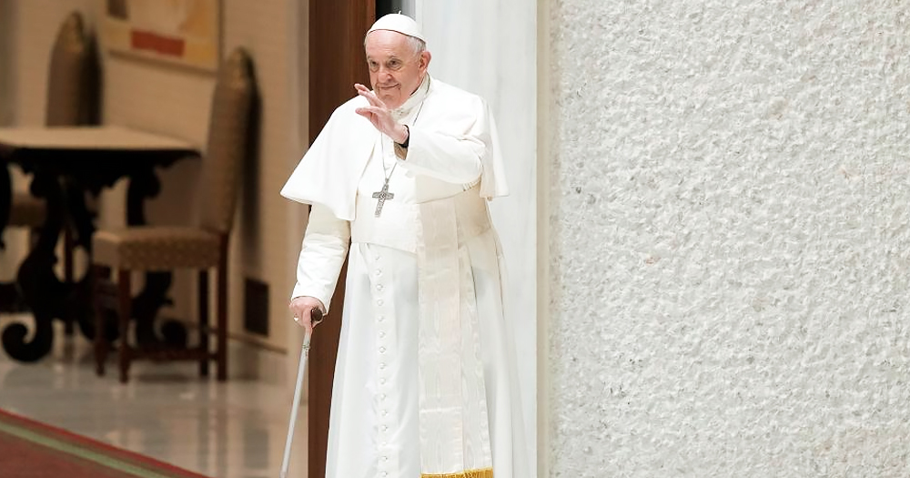 A photo of Pope Francis, who recently met a Trans group, walking and raising his hand.