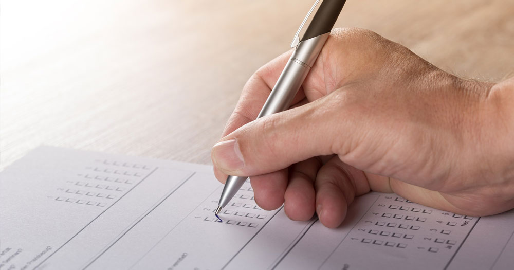 Close up of a hand holding a pen and filling out a survey