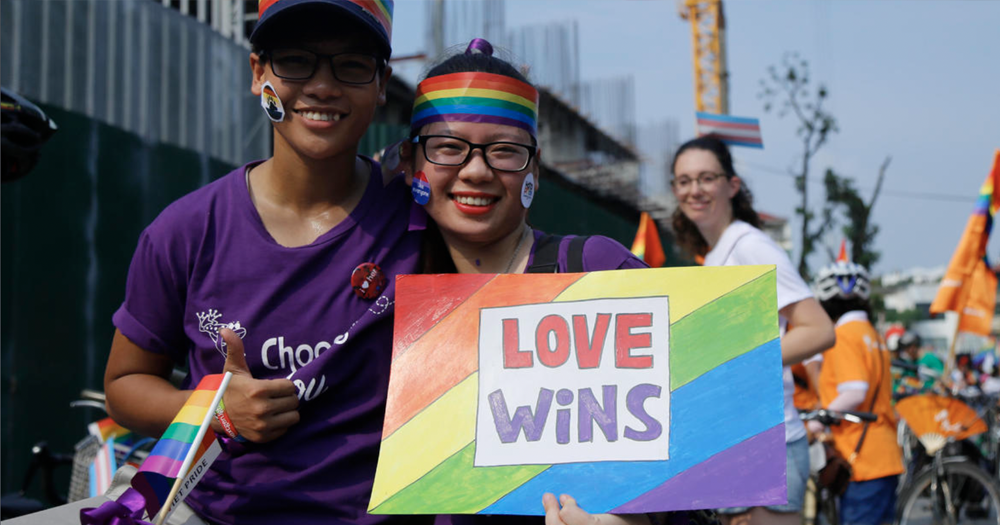 Two people celebrate LGBTQ+ Pride in Vietnam, smiling and posing for the camera and holding a 'love wins' sign