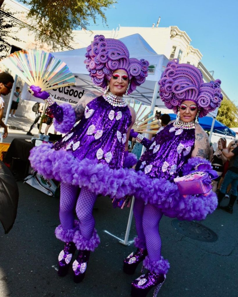 Two people dessed in purple wigs and dresses.